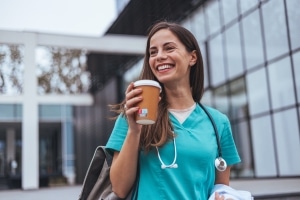 Smiling nurse holding a cup of coffee outside