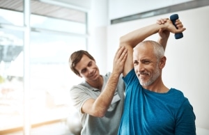 Older man smiling and lifting hand weights in physical therapy