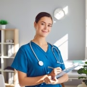 Happy nurse smiling as she writes on a clipboard